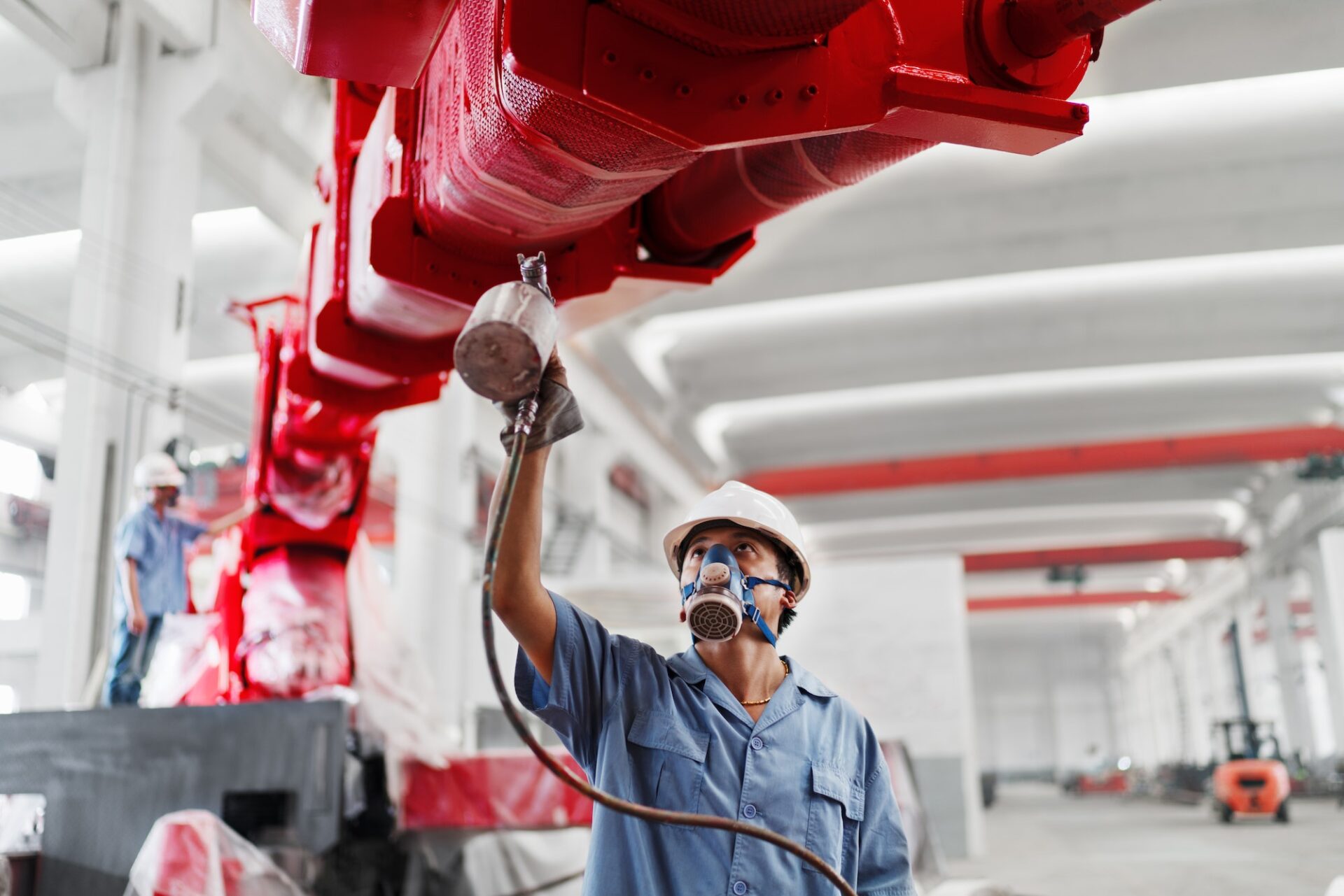 Male workers spray painting a crane arm red in factory workshop, China