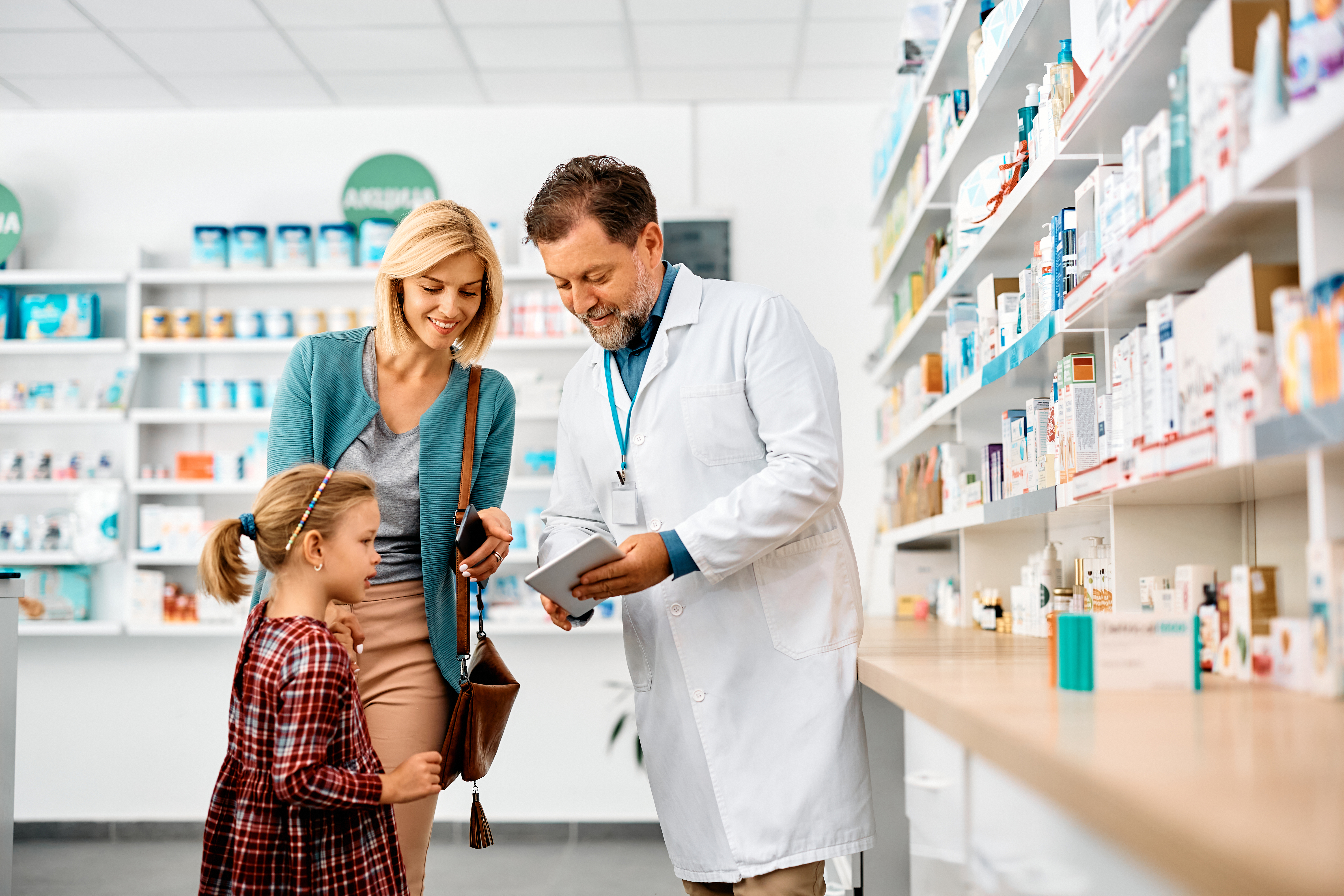 Happy mother and daughter using touchpad with their pharmacist in a pharmacy,