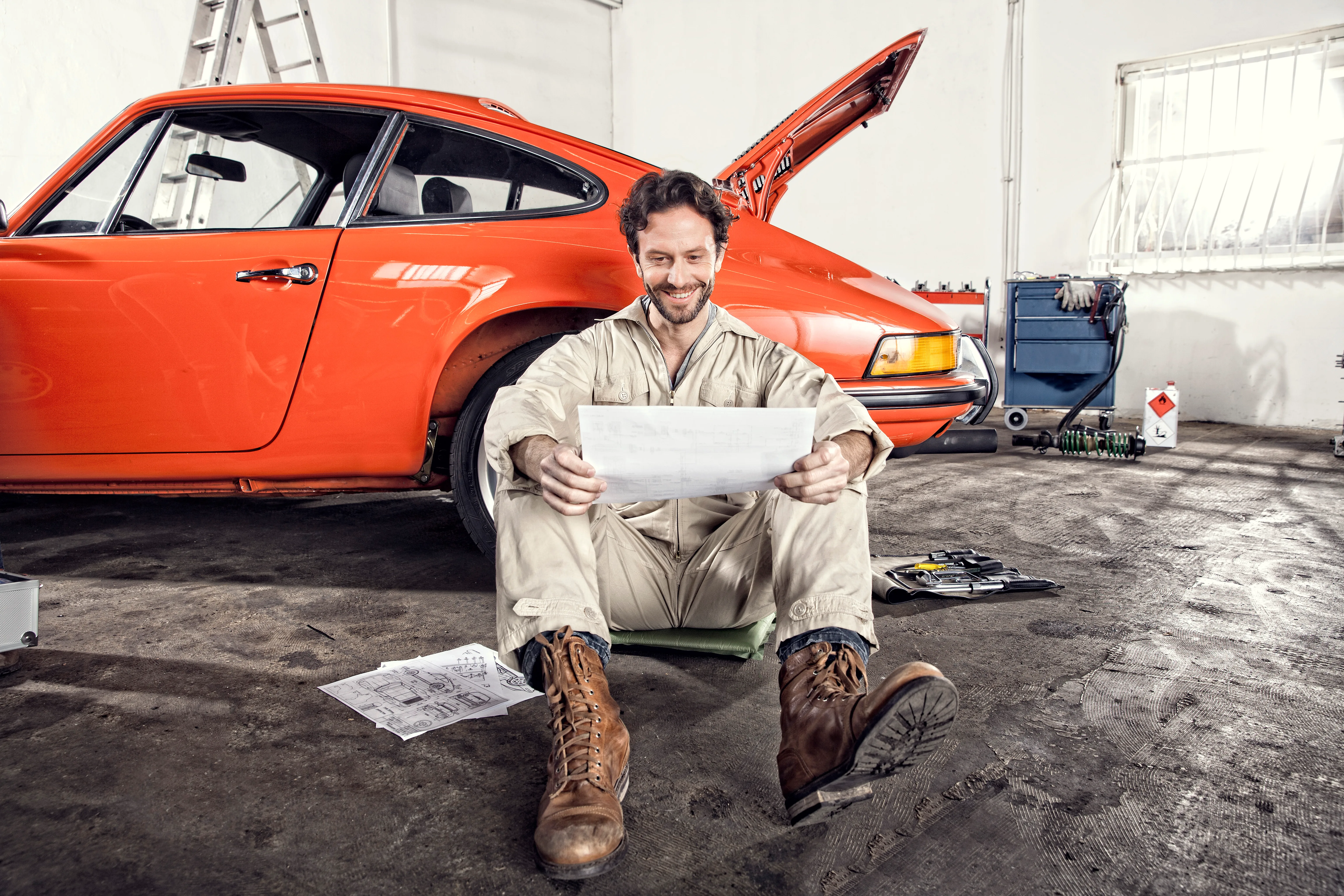 Smiling man with construction plan leaning against his vintage car